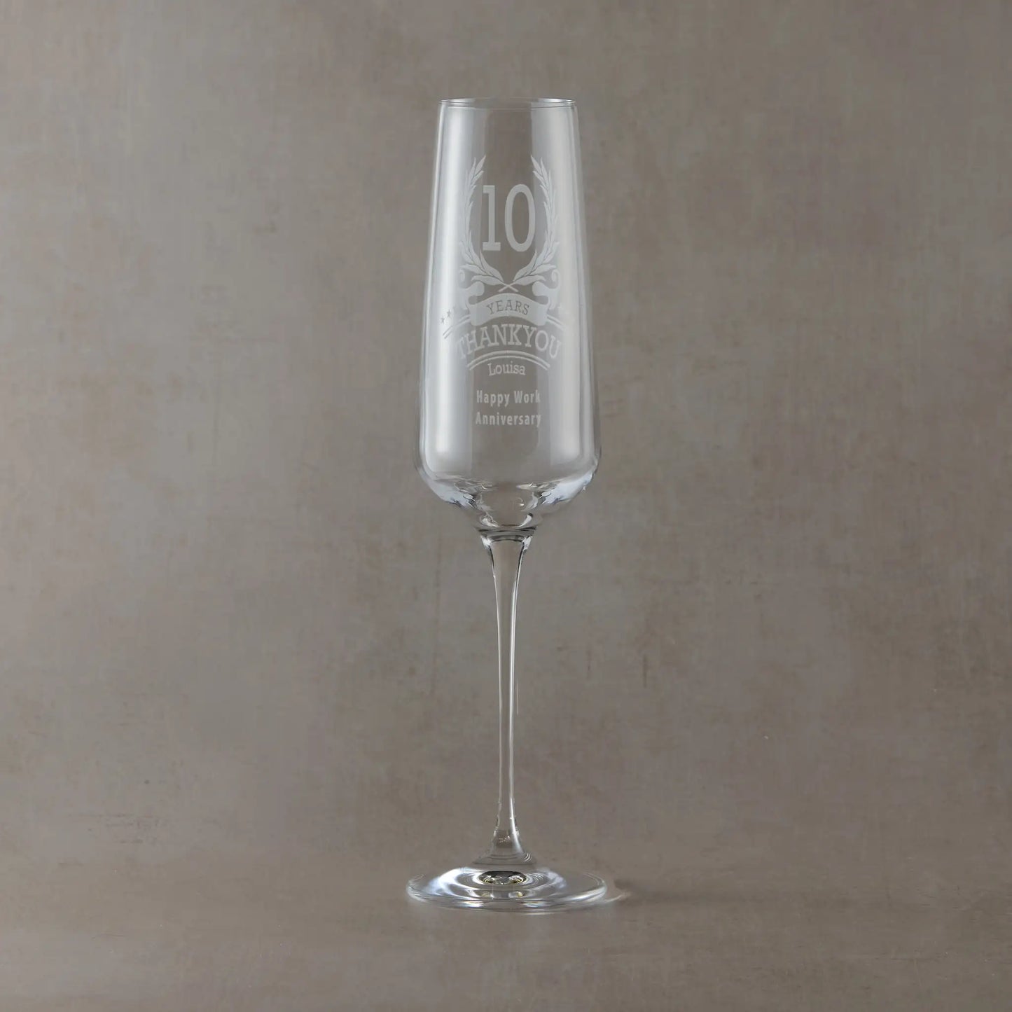 Personalised champagne flute engraved with laurel wreath anniversary design and thankyou message, on a pale background