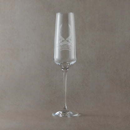 Champagne flute engraved with laurel wreath, ribbon anniversary design and thankyou photographed on a beige background
