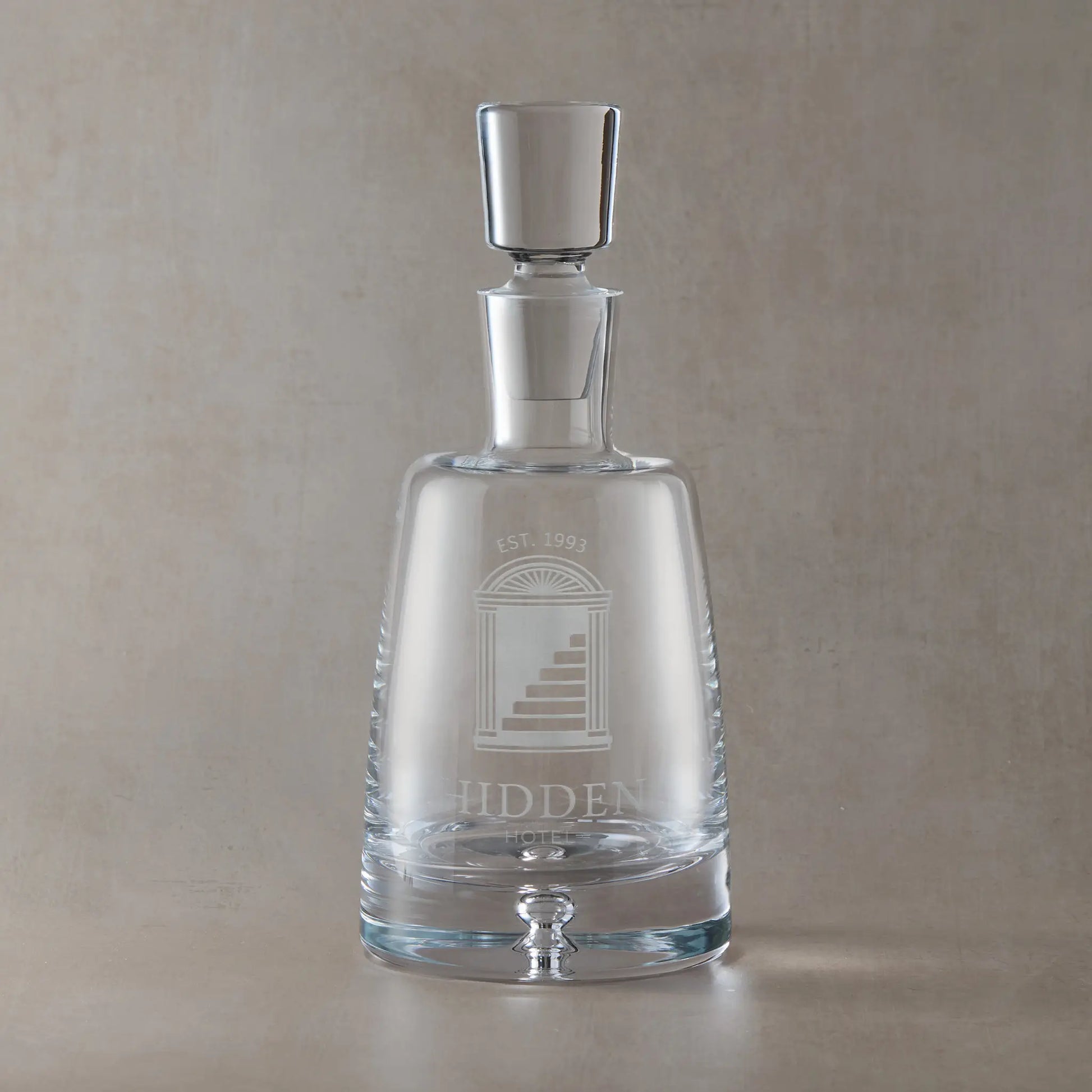 Handmade engraved Atelier spirit decanter featuring a fully custom corporate logo, sandblasted onto clear glass against a neutral beige studio background