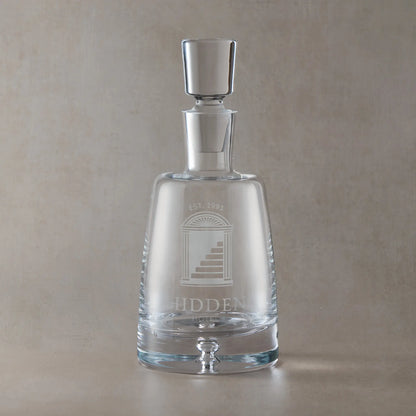 Handmade engraved Atelier spirit decanter featuring a fully custom corporate logo, sandblasted onto clear glass against a neutral beige studio background