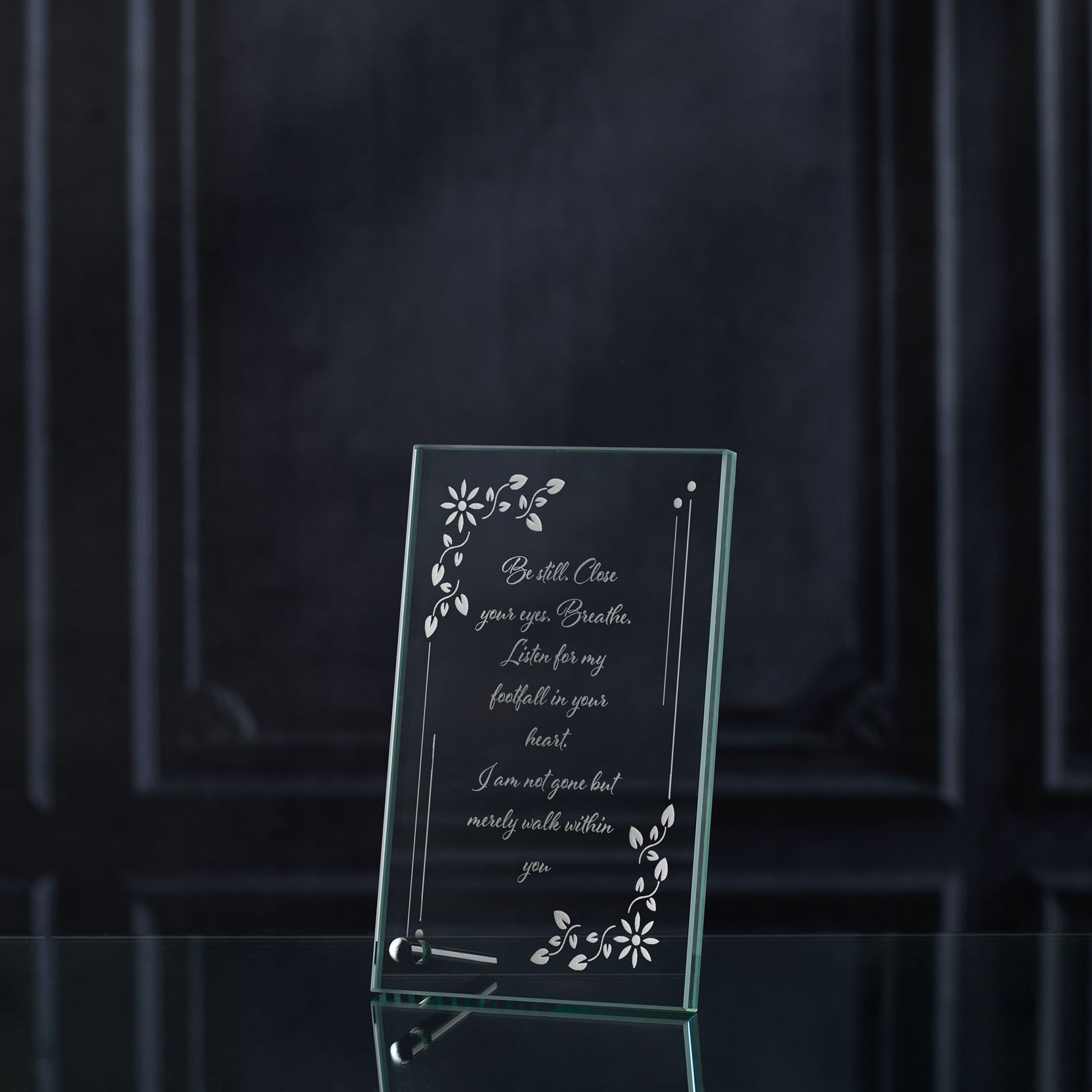 Glass memorial plaque with engraved text and floral designs on a dark background