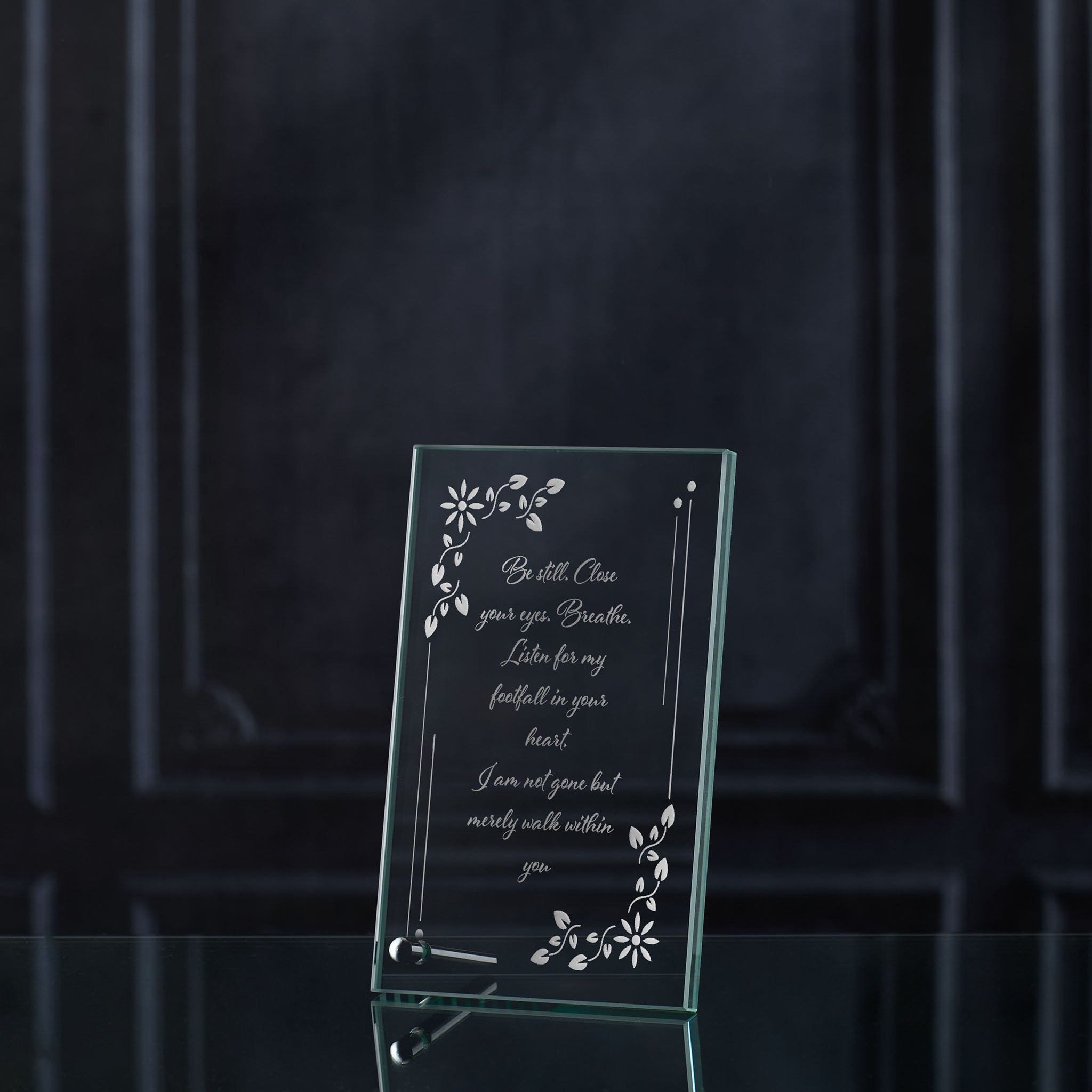 Glass memorial plaque with engraved text and floral designs on a dark background