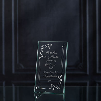 Glass memorial plaque with engraved text and floral designs on a dark background