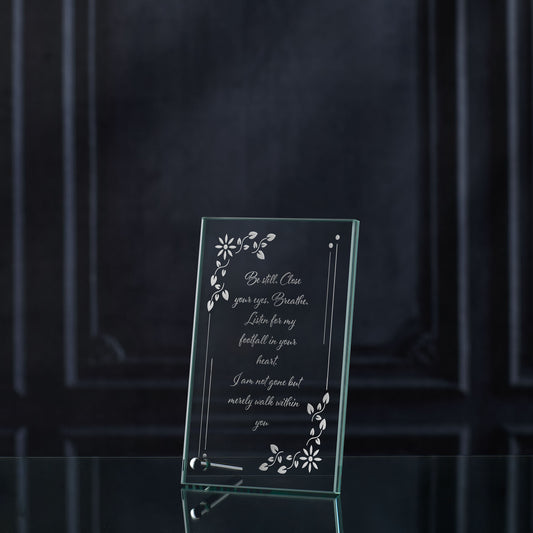 Glass memorial plaque with engraved text and floral designs on a dark background