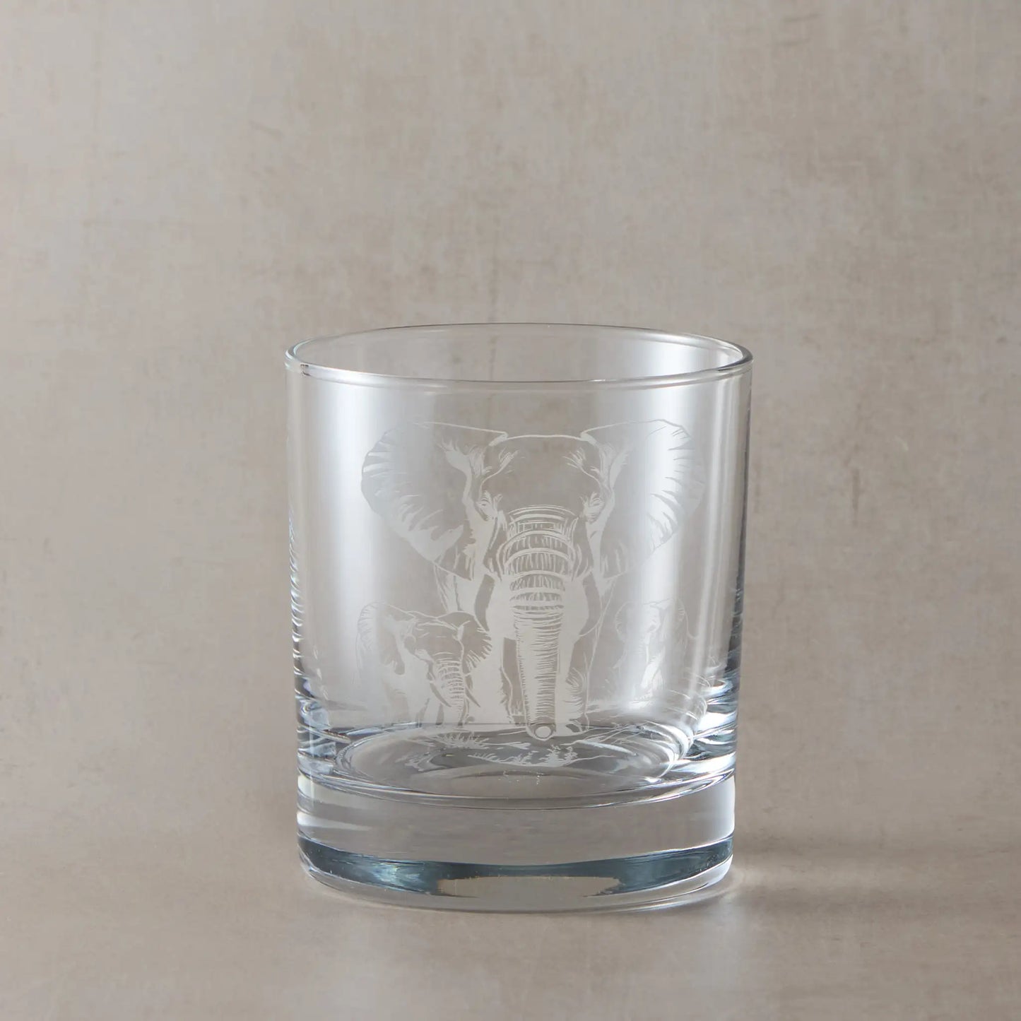 Whisky glass engraved with an Elephant and two calves, photographed on a beige background