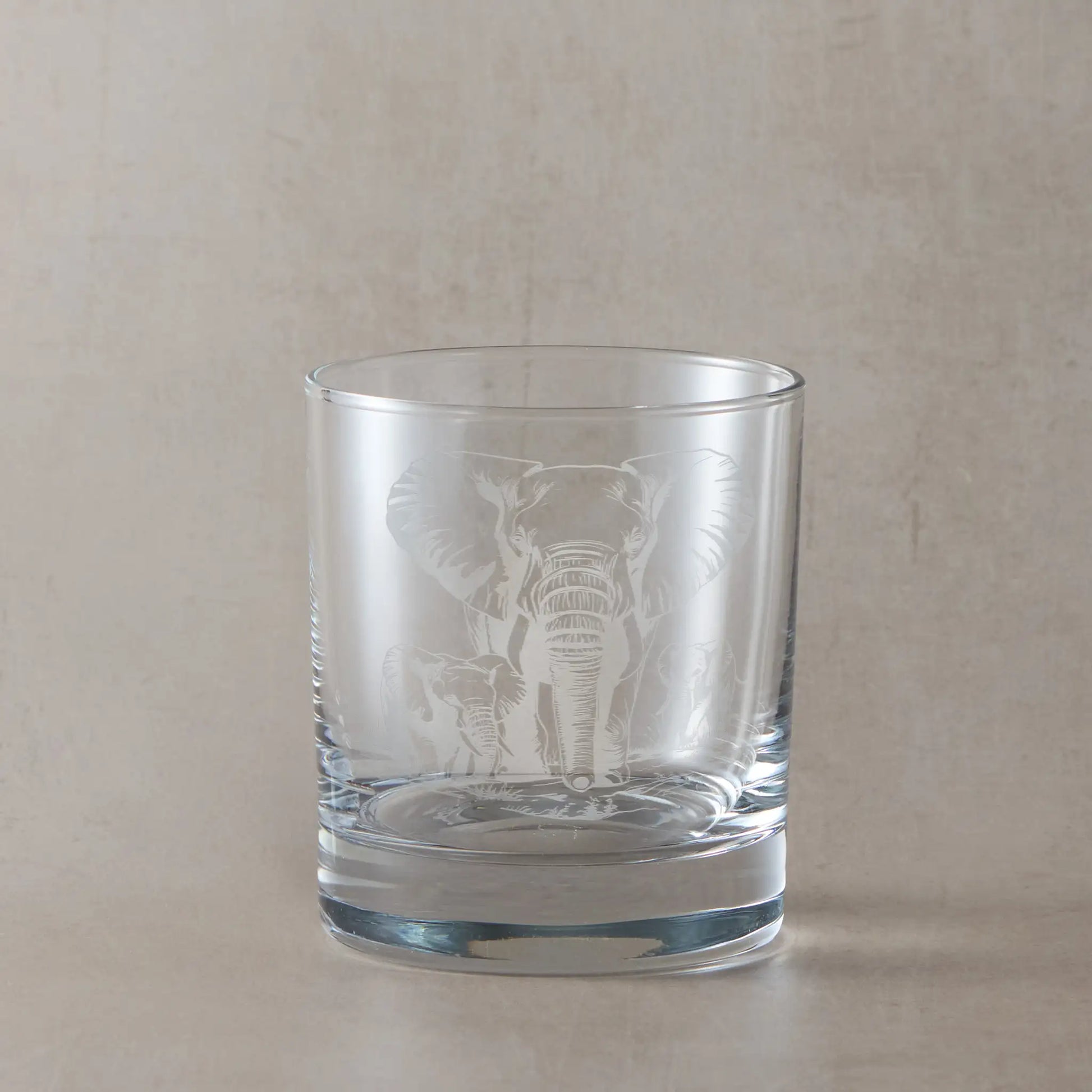 Whisky glass engraved with an Elephant and two calves, photographed on a beige background