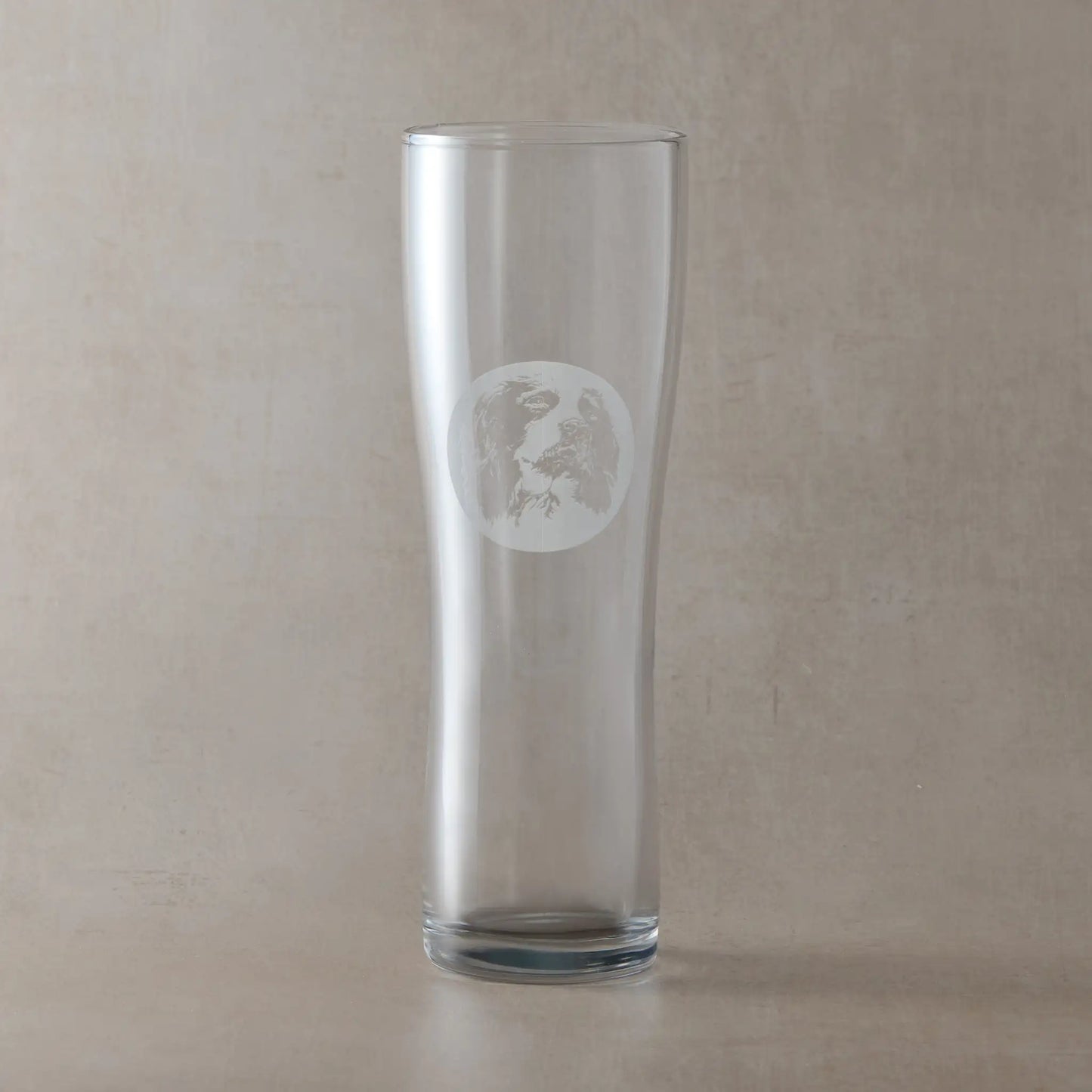 Pint glass engraved with a portrait of a Springer Spaniel shown against a neutral beige background.