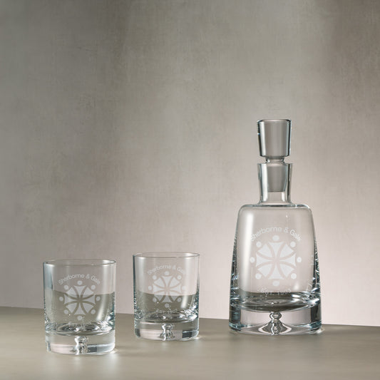 A crystal decanter with a stopper and two matching whisky glasses, all engraved with a corporate branded logo design