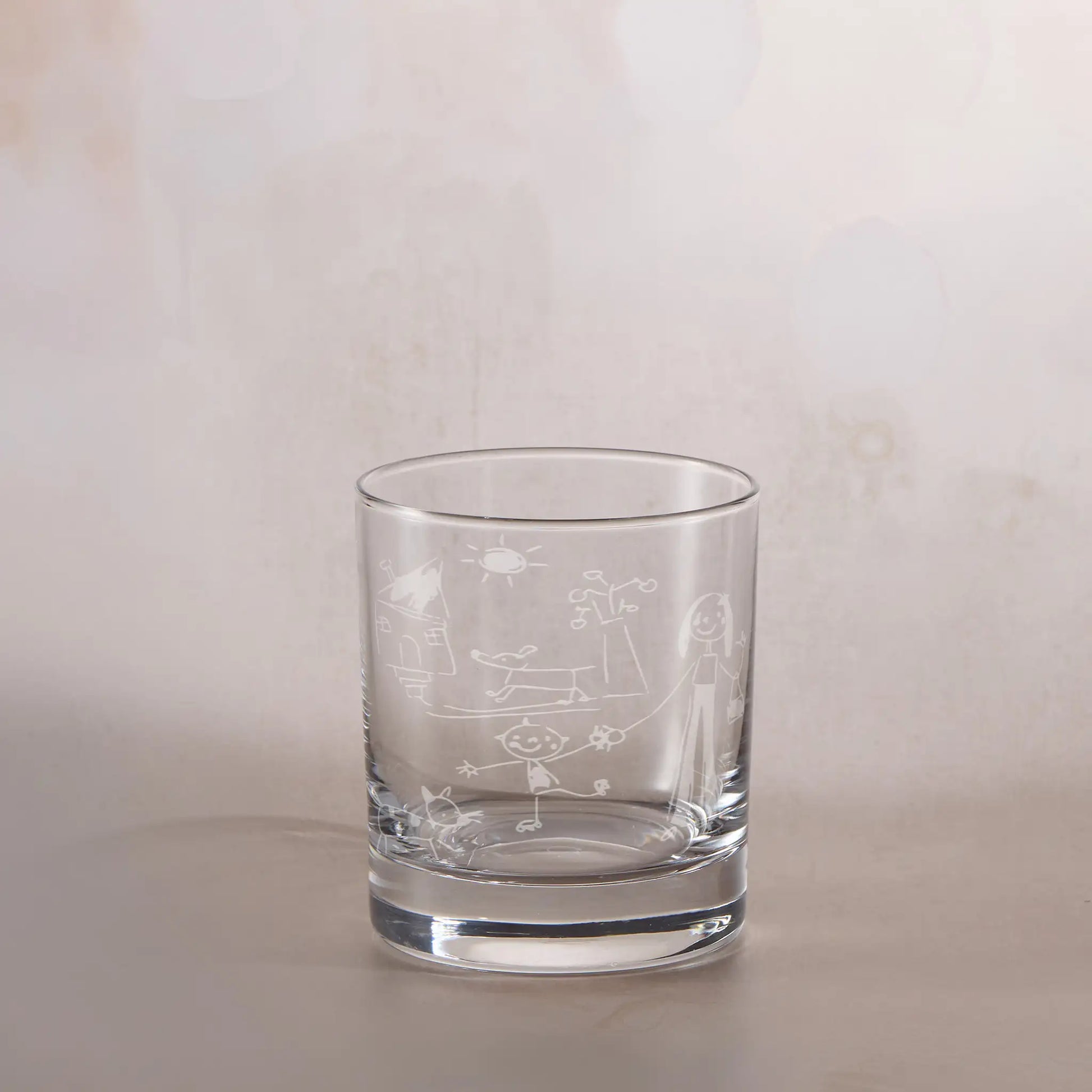 Clear glass tumbler with engraved childs drawing on a beige background