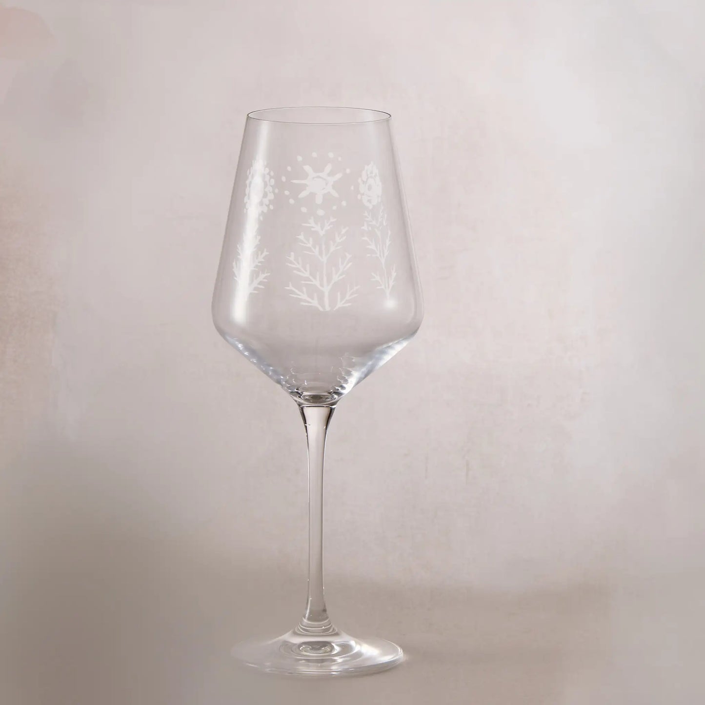 Clear wine glass with engraved childs drawing on a light gray background