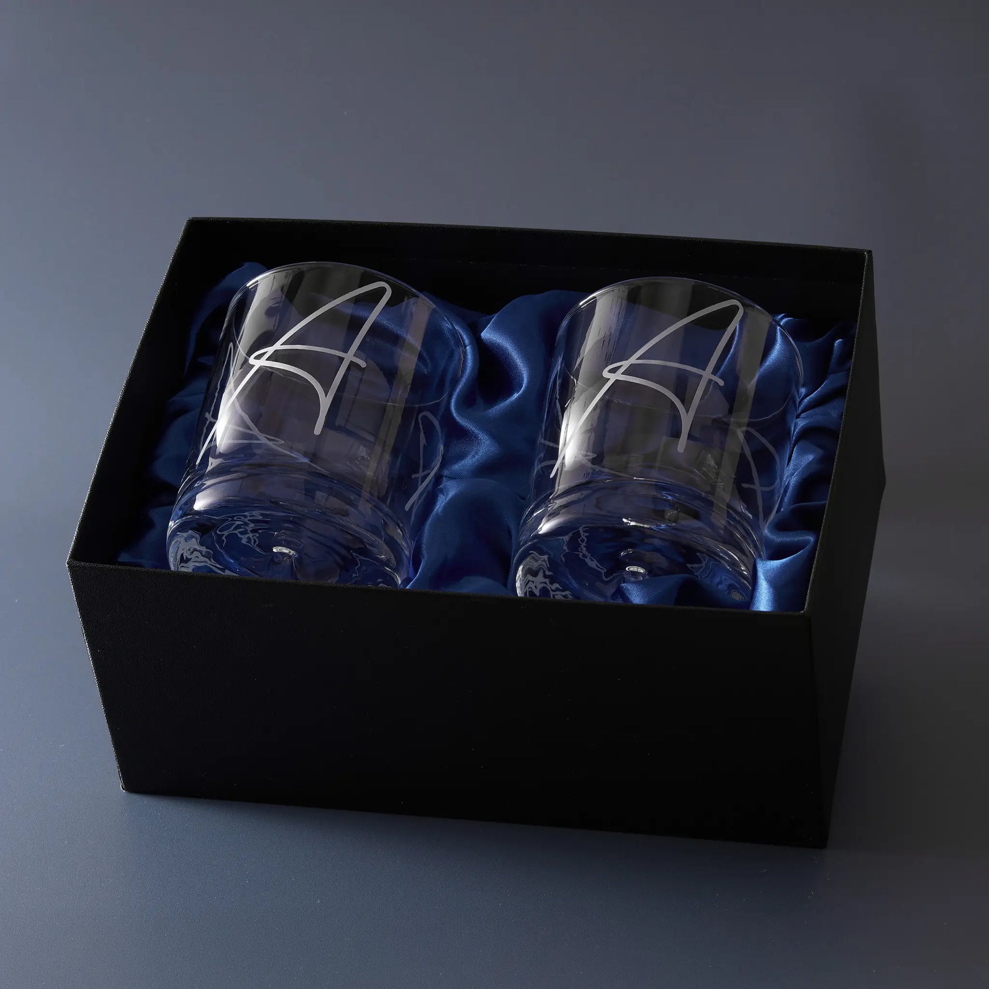Two engraved whisky glasses with a monogram in a black box lined with blue satin