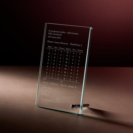 Glass display plaque with engraved golf scorecard, photographed on a dark, softly lit background