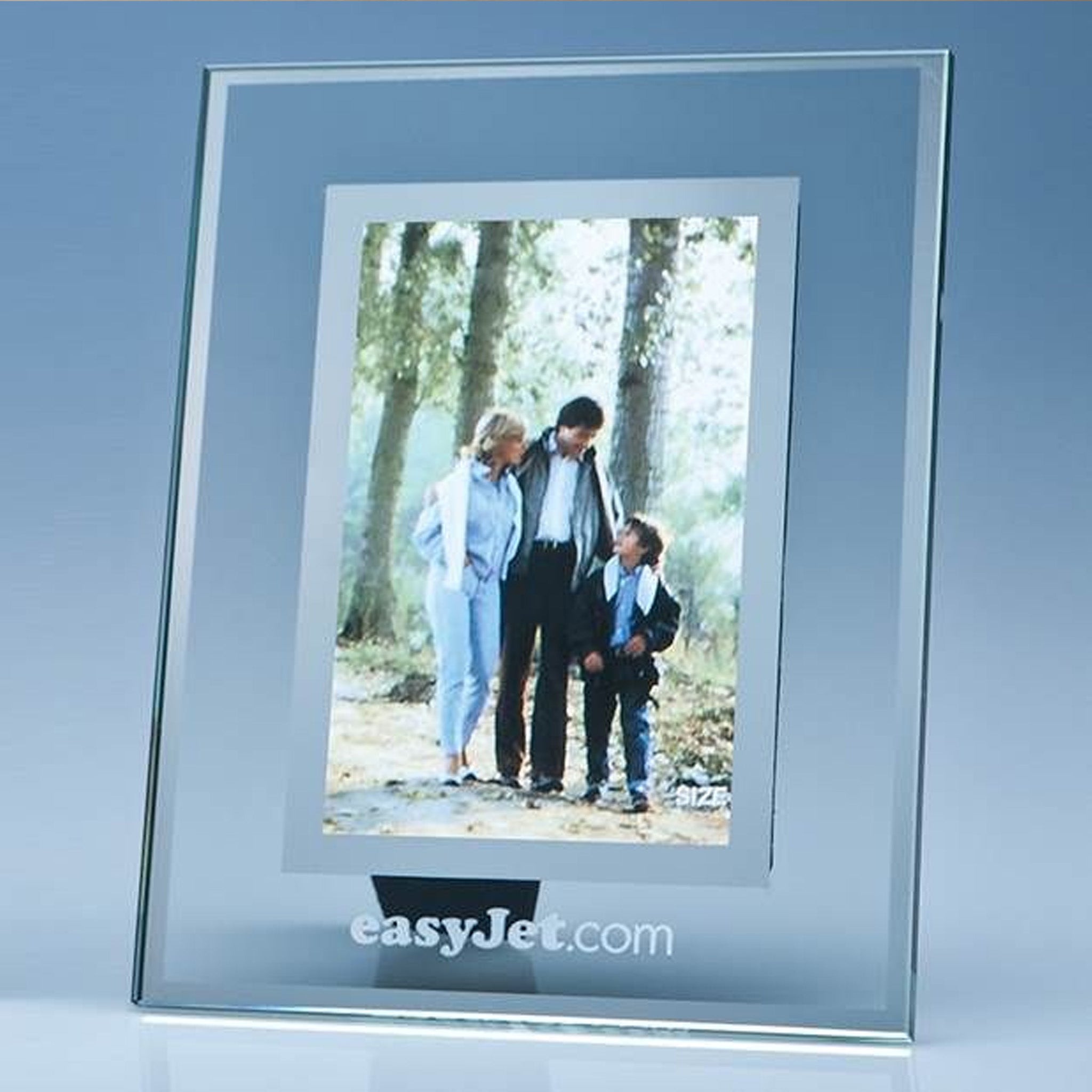 A clear acrylic picture frame with a silver-toned border and a sample family photograph inside, standing on a reflective surface against a blue-gray gradient background. The text 'easyJet.
