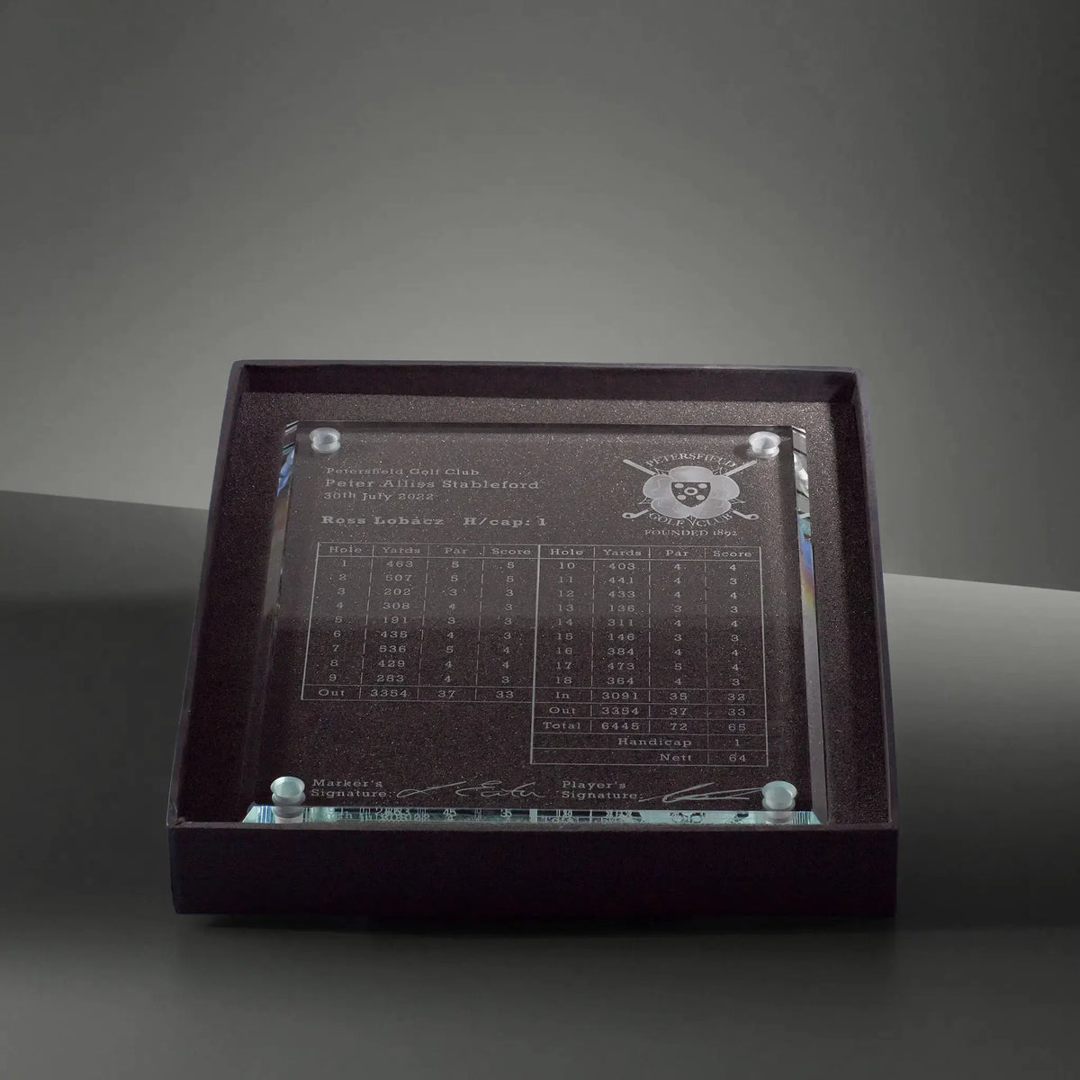 Clear glass plaque with engraved scorecard text, signatures, and a small golf crest presented in a lined presentation box