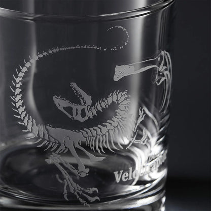 Clear glass tumbler with engraved dinosaur skeleton design and 'Velociraptor' text.