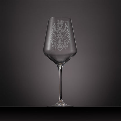 A clear glass wine glass with an etched ornate Welsh lovespoon design on the bowl.