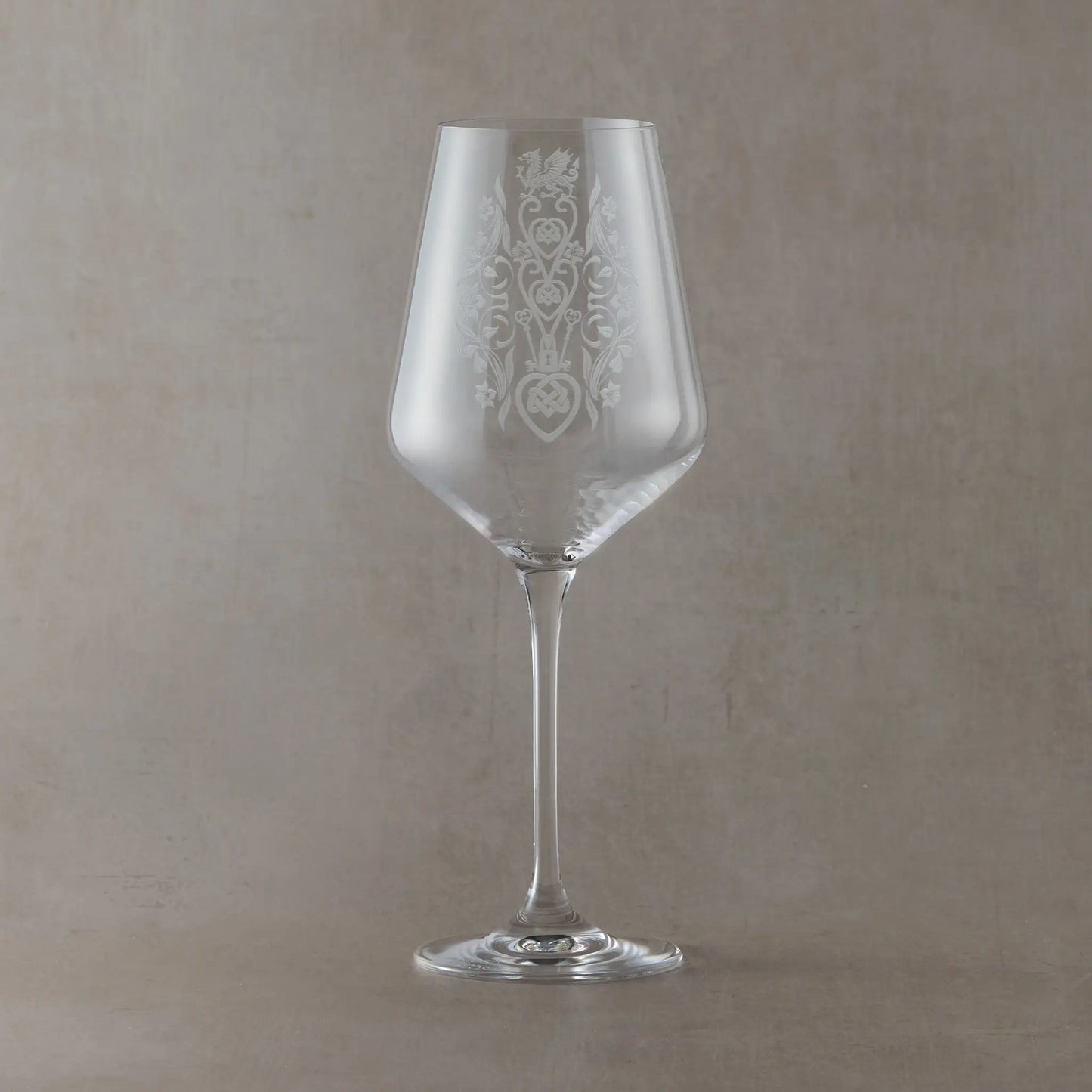 A clear wine glass with an etched floral welsh lovespoon design on the bowl