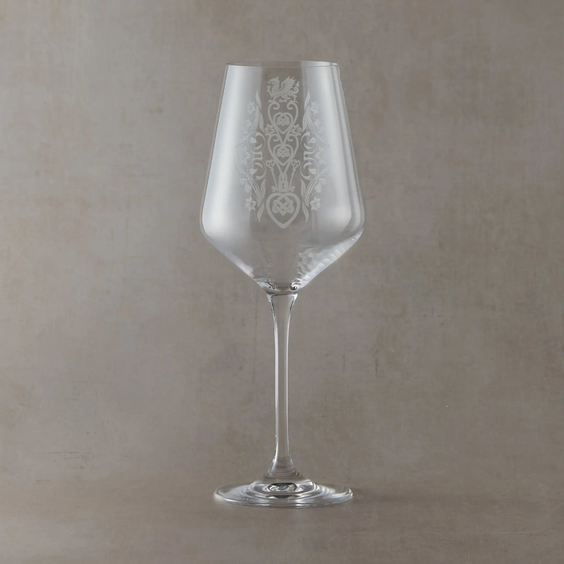 A clear wine glass with an etched floral welsh lovespoon design on the bowl