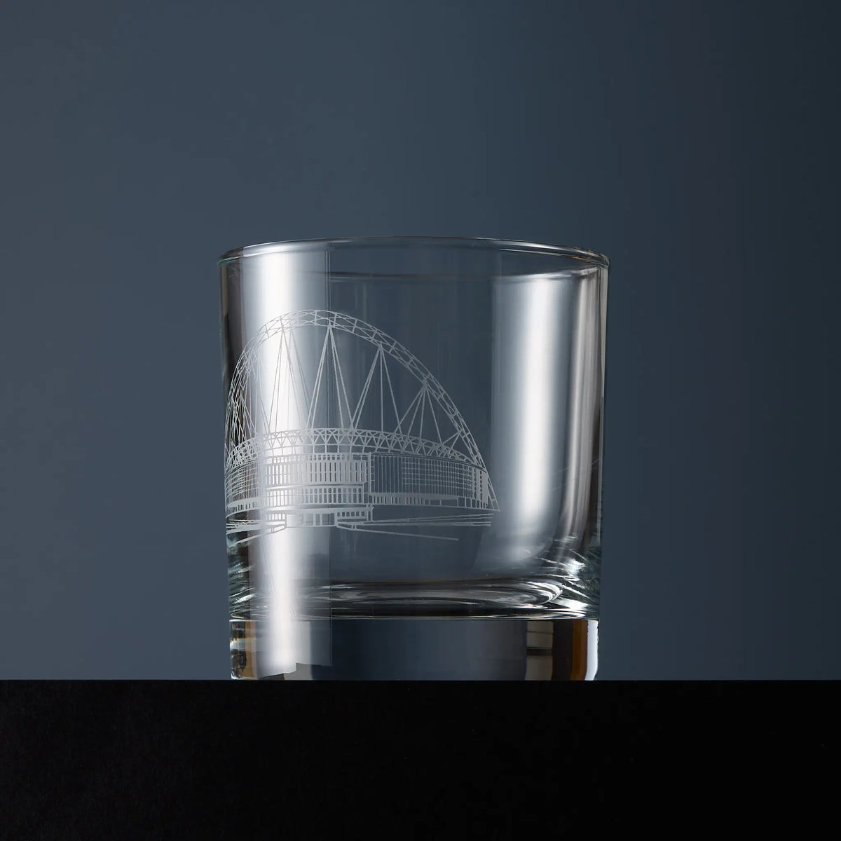 A clear glass whisky tumbler with an etched line drawing of Wembley stadium.