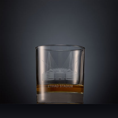 Engraved whisky glass featuring a line-art illustration of the Etihad Stadium, shown on a dark background to highlight the fine detail of the sandblasted engraving.