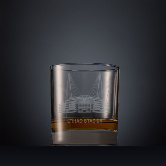 Engraved whisky glass featuring a line-art illustration of the Etihad Stadium, shown on a dark background to highlight the fine detail of the sandblasted engraving.