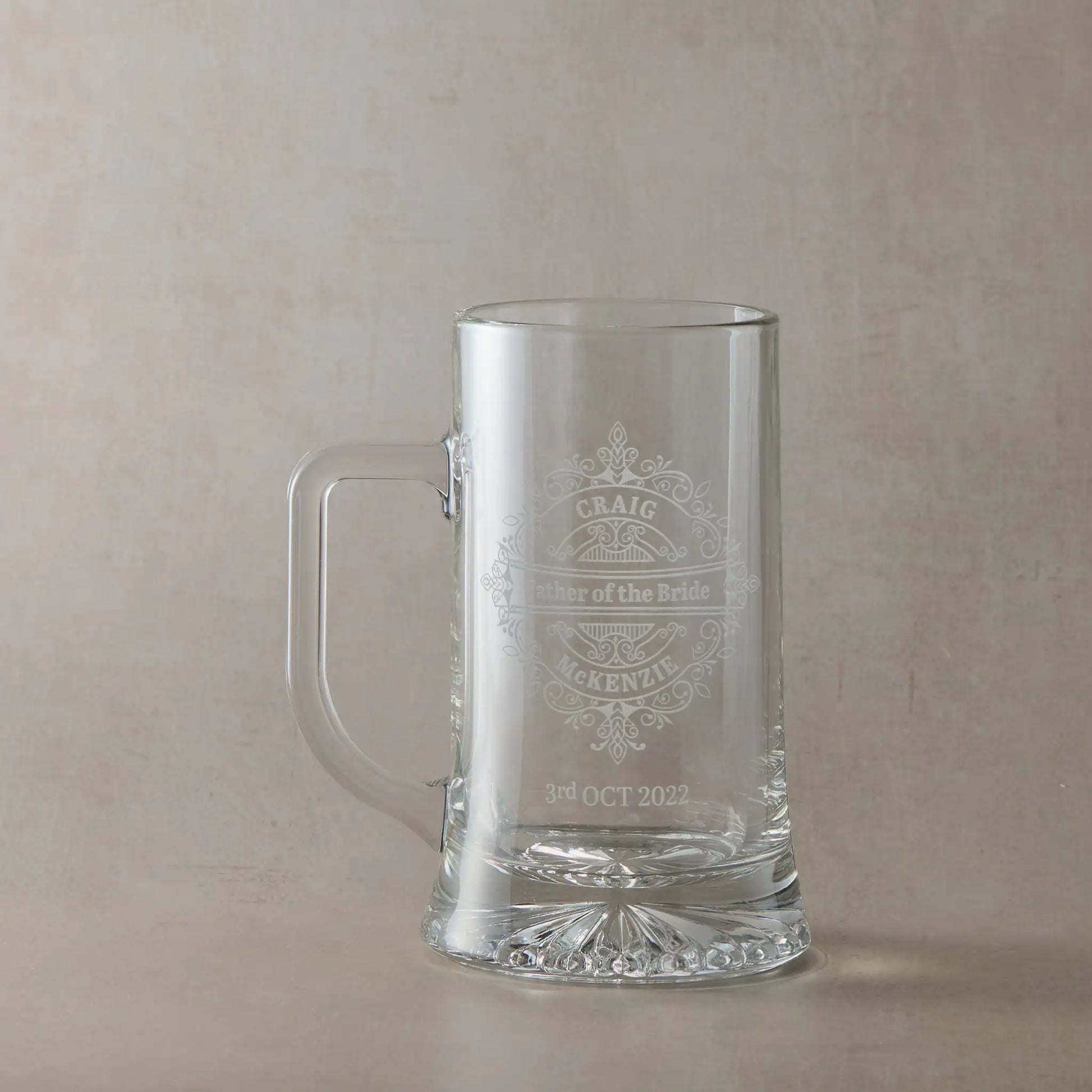 Father of the bride engraved glass tankard personalised with names and date, ona plae background.