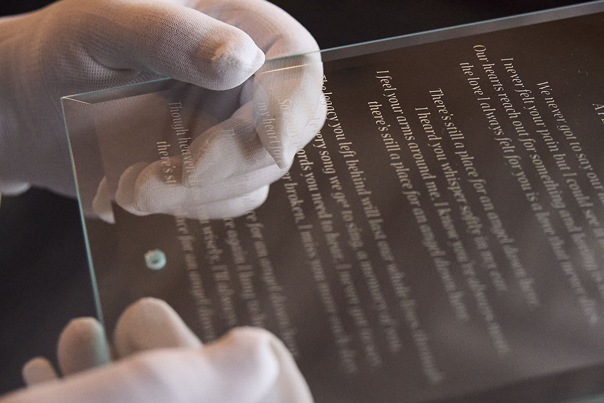 Person wearing gloves holding a transparent display plaque with engraved text