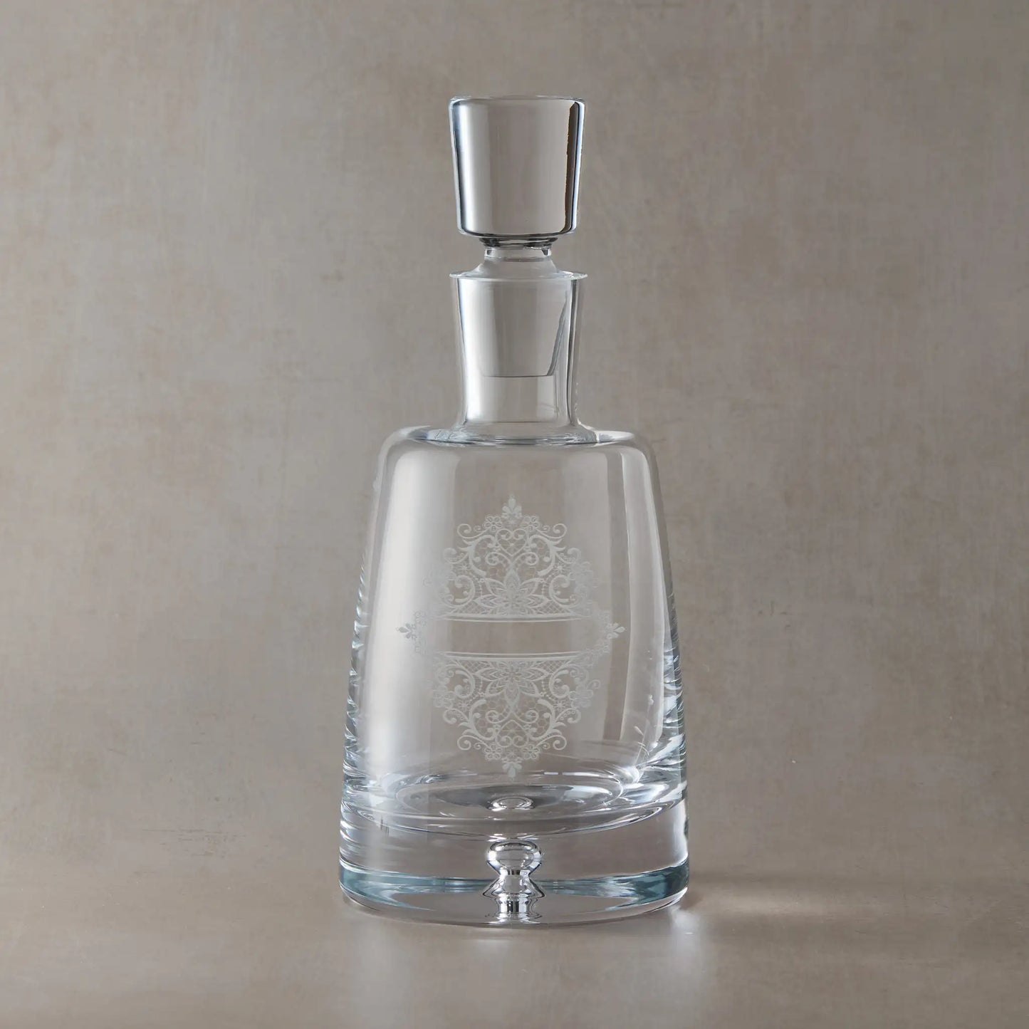 Glass decanter engraved with a floral guipure lacework design, photographed on a beige background