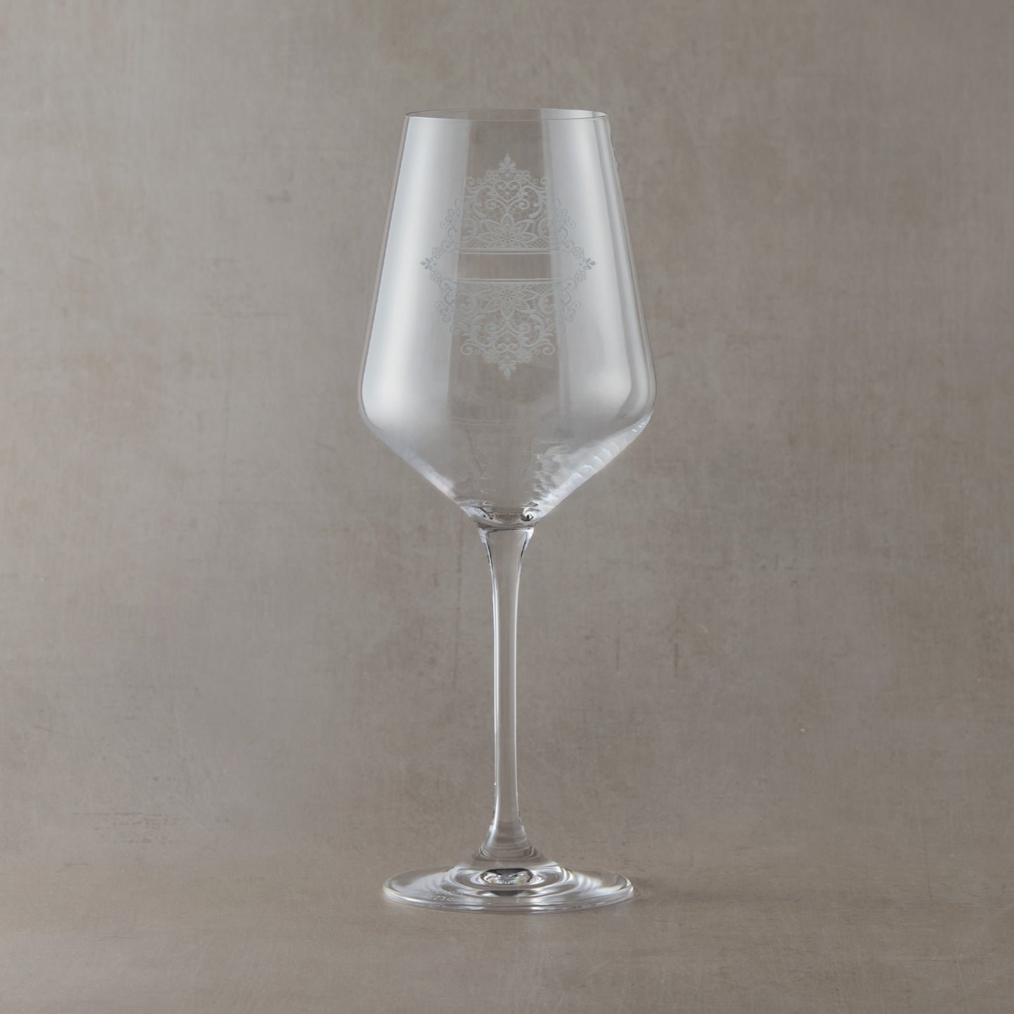 Clear wine glass with intricate guipure lace engraved design on a beige background