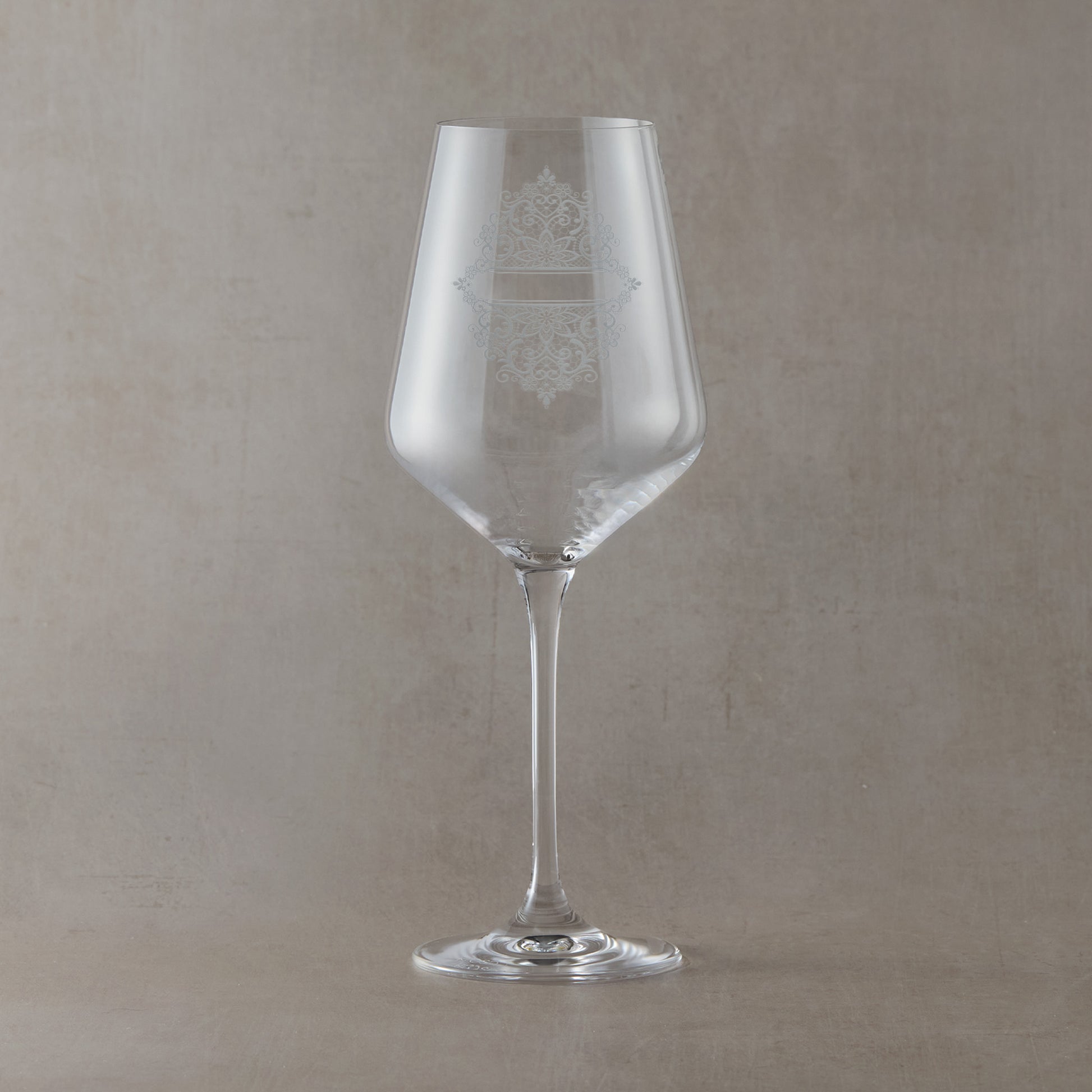 Clear wine glass with intricate guipure lace engraved design on a beige background