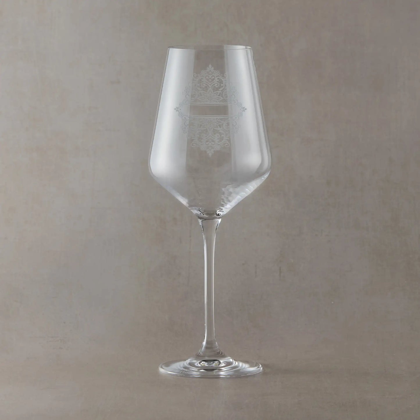 Clear wine glass with an engraved lacework design on a beige background