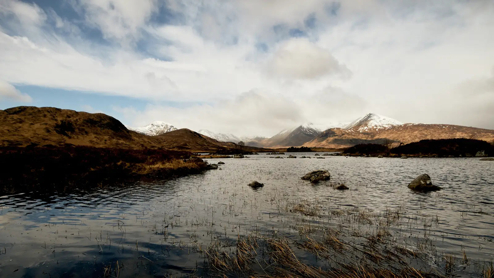 Scenic view of a loch with Glencoe mountains in the background under a cloudy sky.