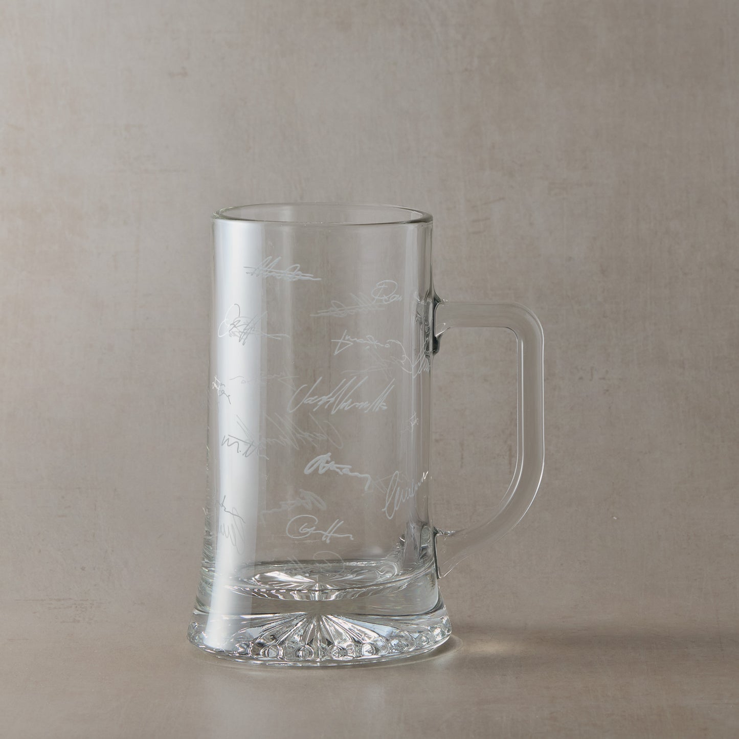 Glass tankard engraved with colleagues handwritten signatures, shown on a beige background.