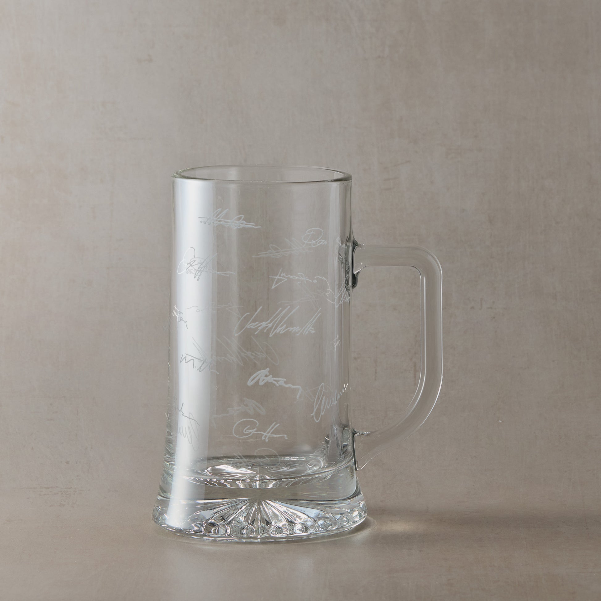 Glass tankard engraved with colleagues handwritten signatures, shown on a beige background.