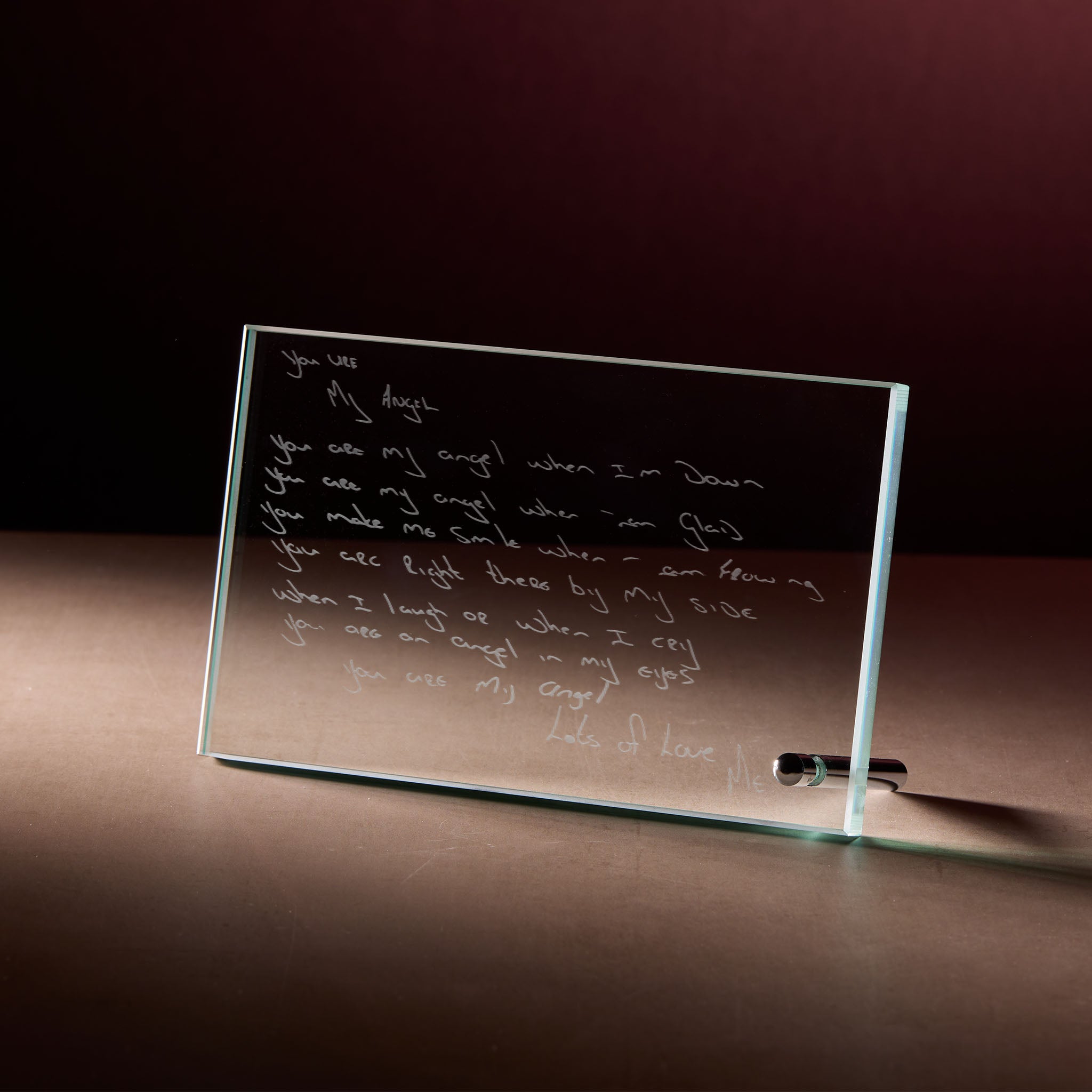 Glass display plaque with engraved handwritten love poem, photographed on a dark, softly lit background