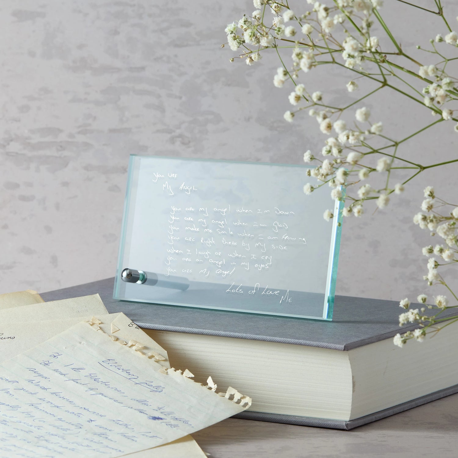 personalised glass plaque with engraved text on a stack of books with white flowers.