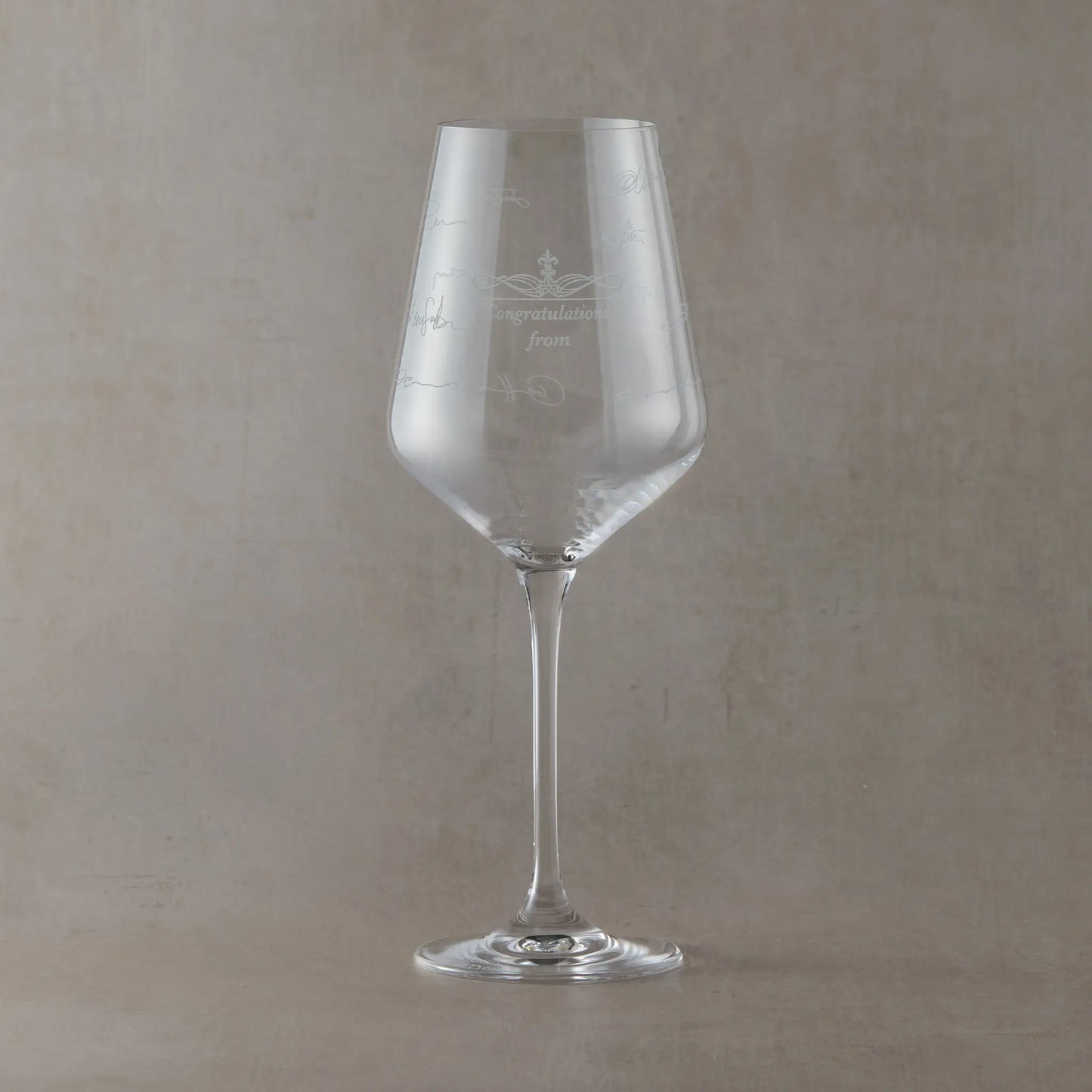 Clear wine glass with engraved handwritten text on a beige background