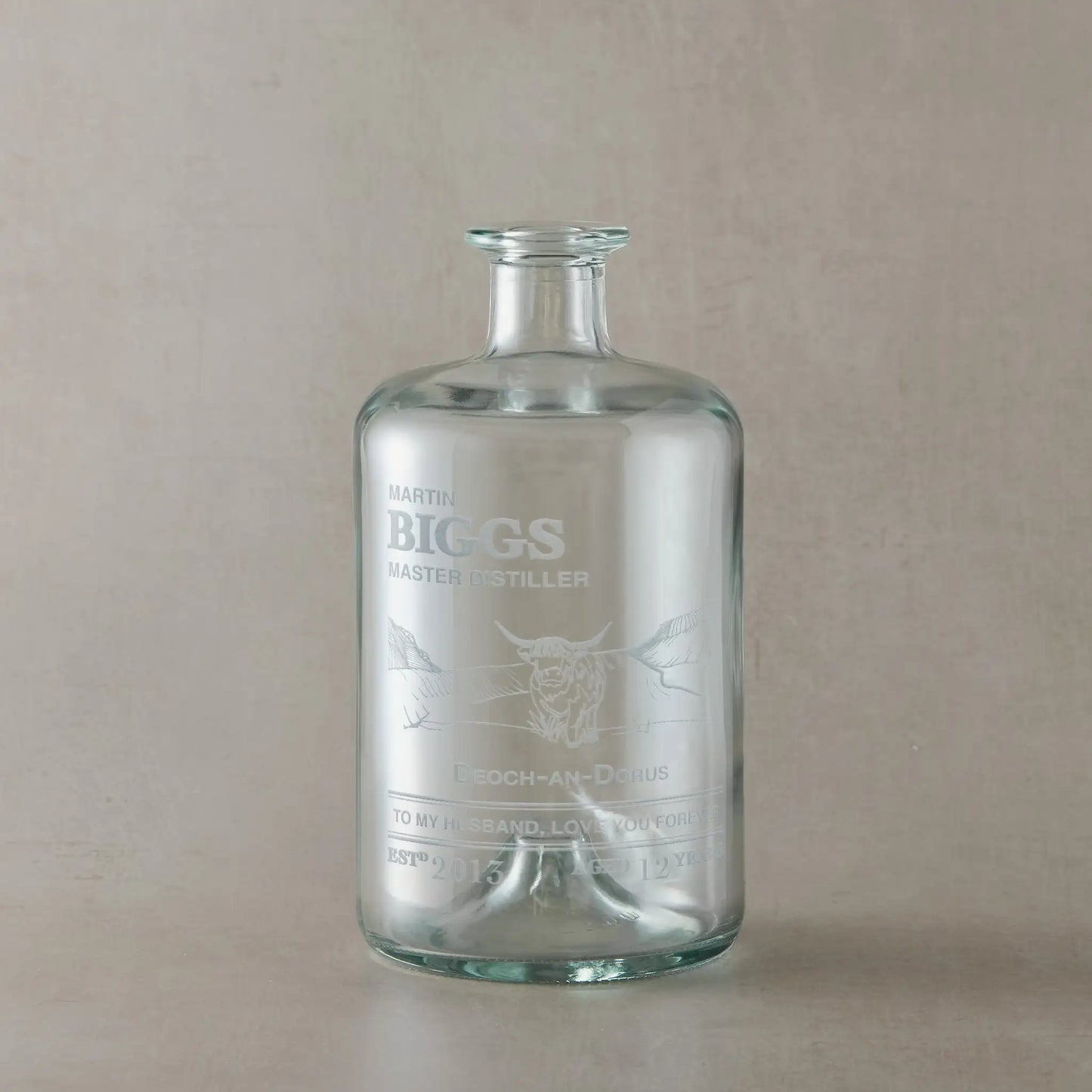 Engraved glass whisky bottle with a highland cow and personalised text on a beige background