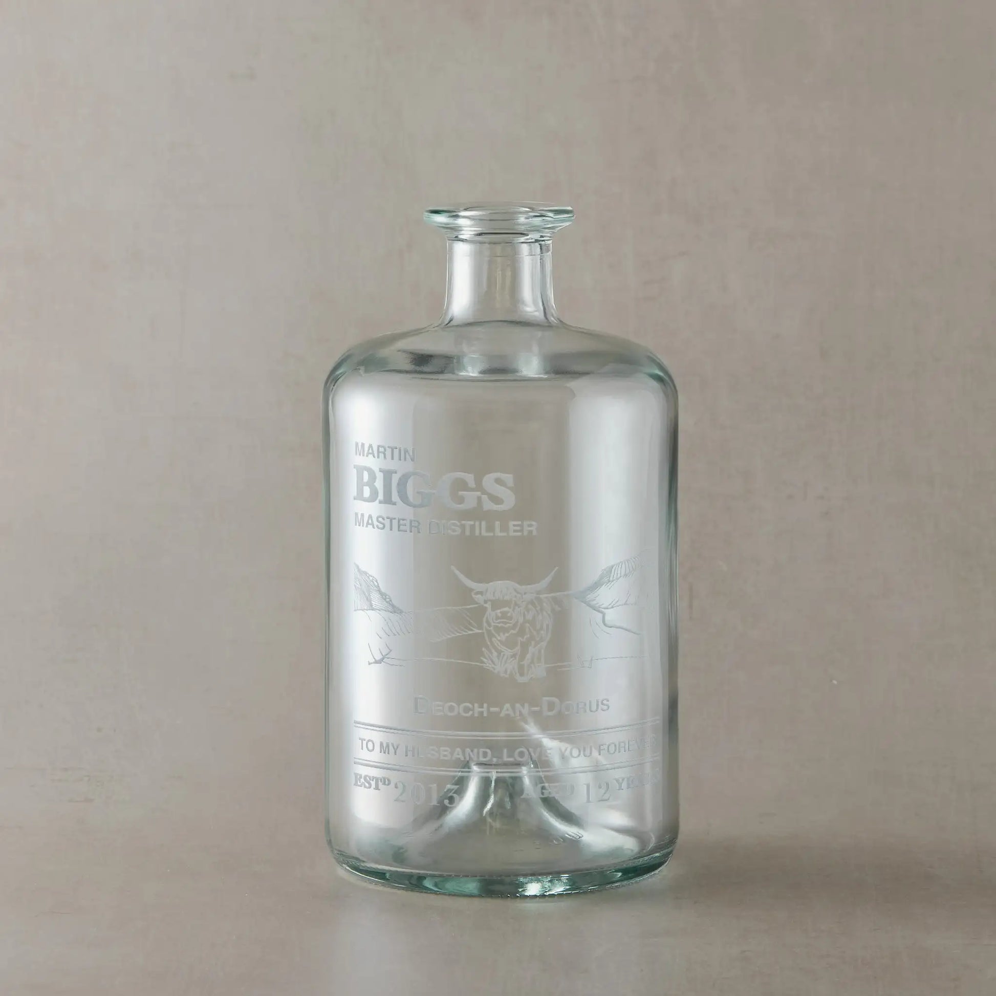 Engraved glass whisky bottle with a highland cow and personalised text on a beige background