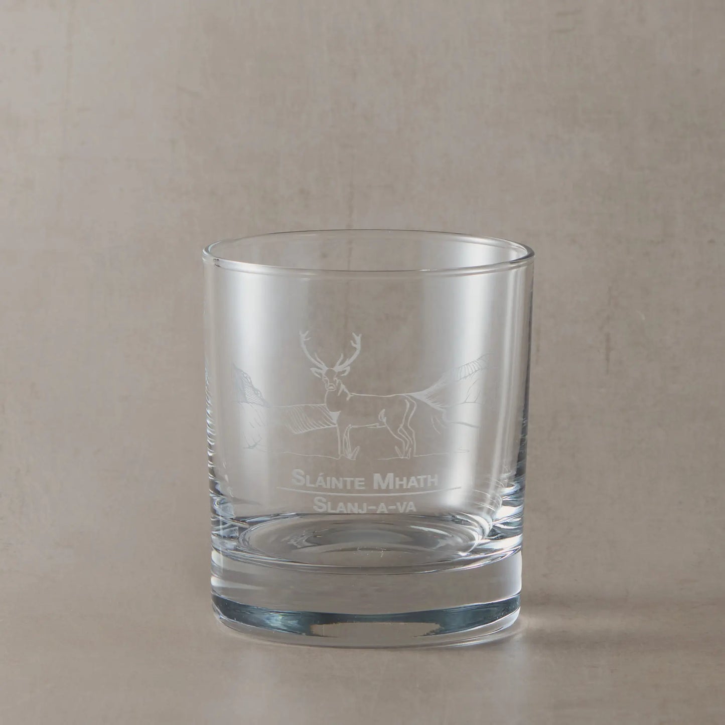 Whisky glass with engraved highland stag and slainte design on a beige background