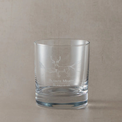 Whisky glass with engraved highland stag and slainte design on a beige background