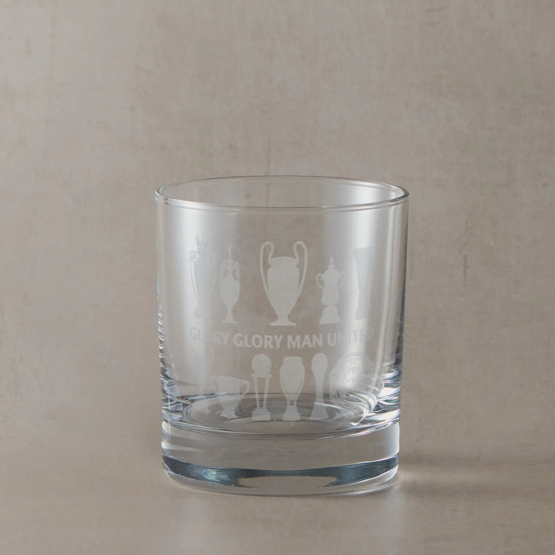 Personalised whisky glass engraved with eleven trophy silhouettes photographed on a beige background