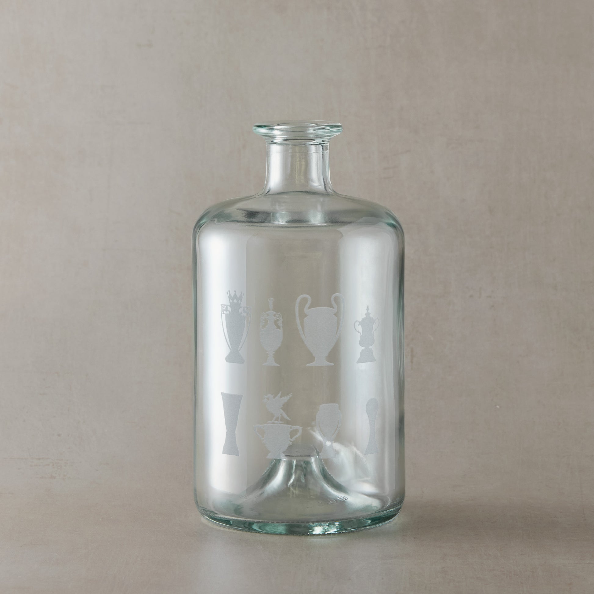 Apothecary-style glass decanter engraved with eight trophy silhouettes and a Liverbird motif, photographed on a beige background