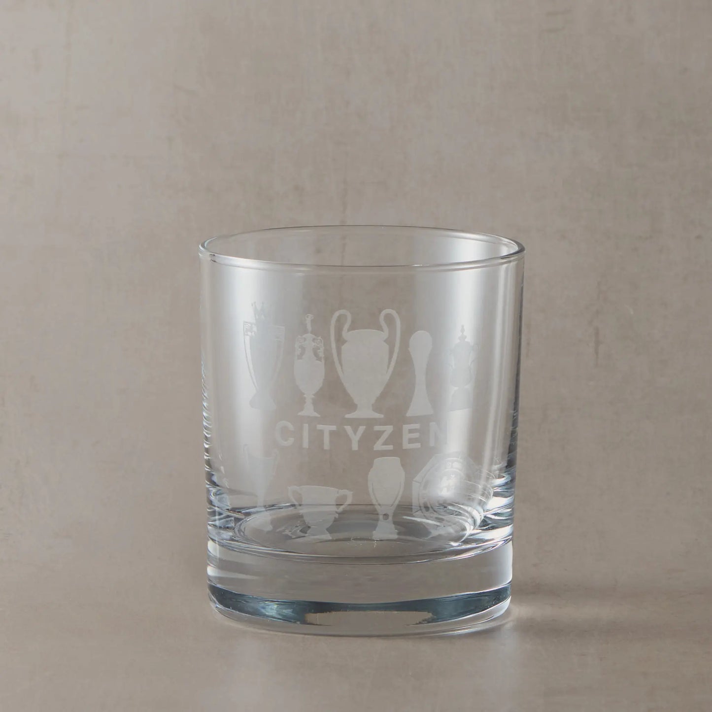 Personalised whisky glass engraved with nine trophy silhouettes photographed on a beige background