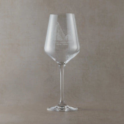 Wine glass with engraved Inaccessible Pinnacle illustration on a beige background