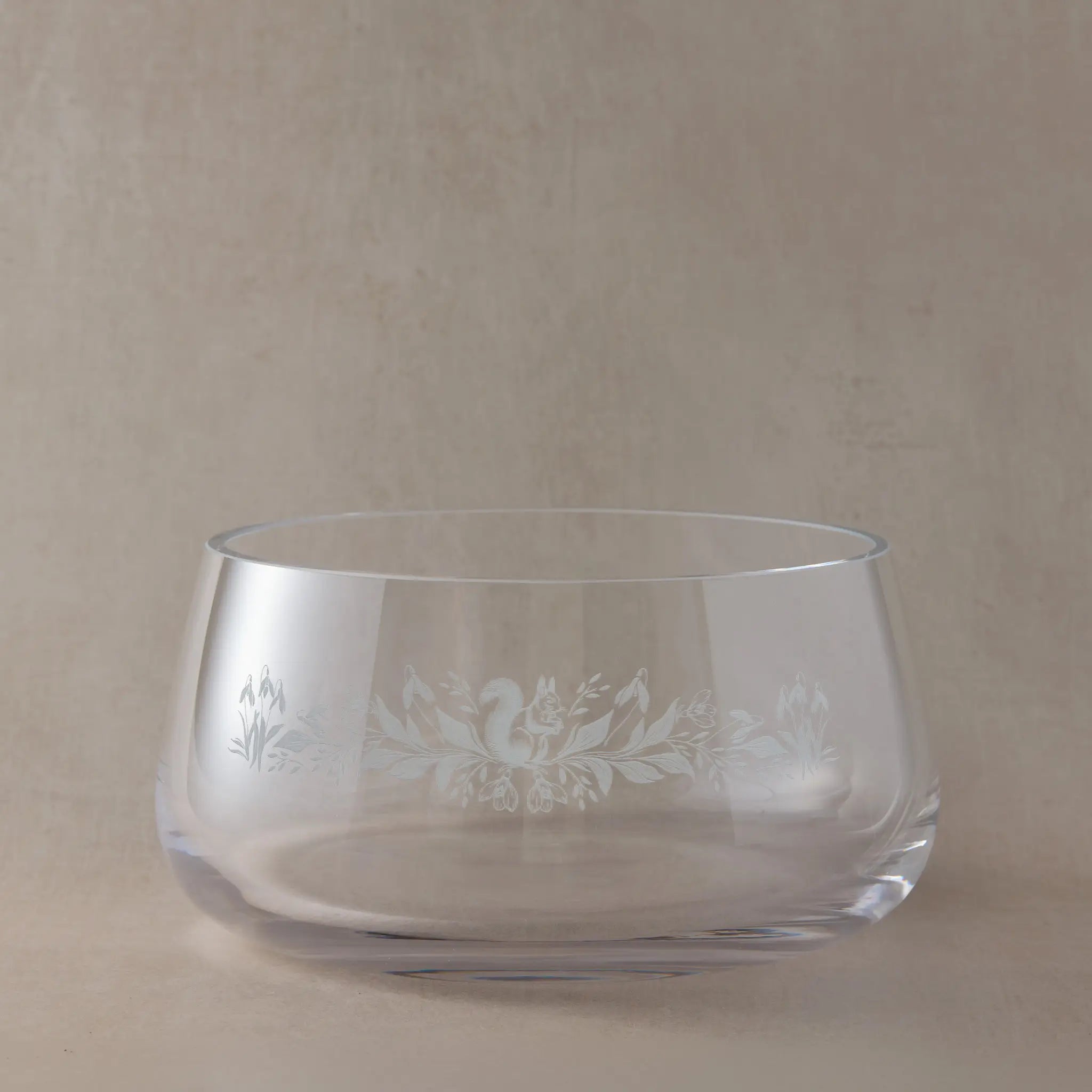 Handmade clear glass fruit bowl engraved with a January birth flowers design featuring snowdrops and a squirrel, shown on a soft neutral studio background