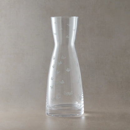 Clear glass carafe with engraved butterfly designs on a beige background