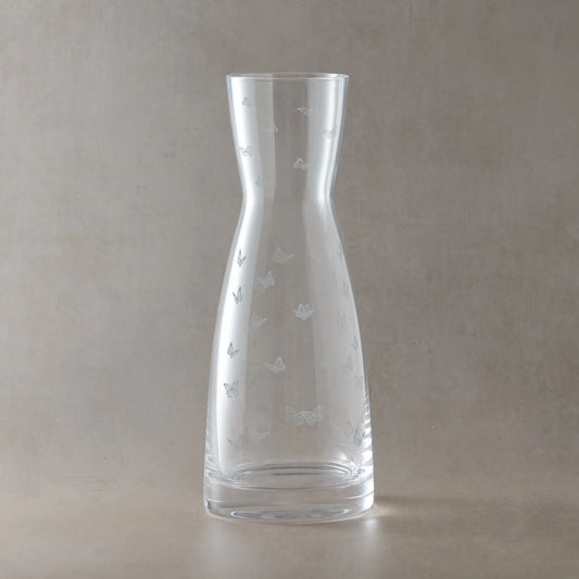 Clear glass carafe with engraved butterfly designs on a beige background