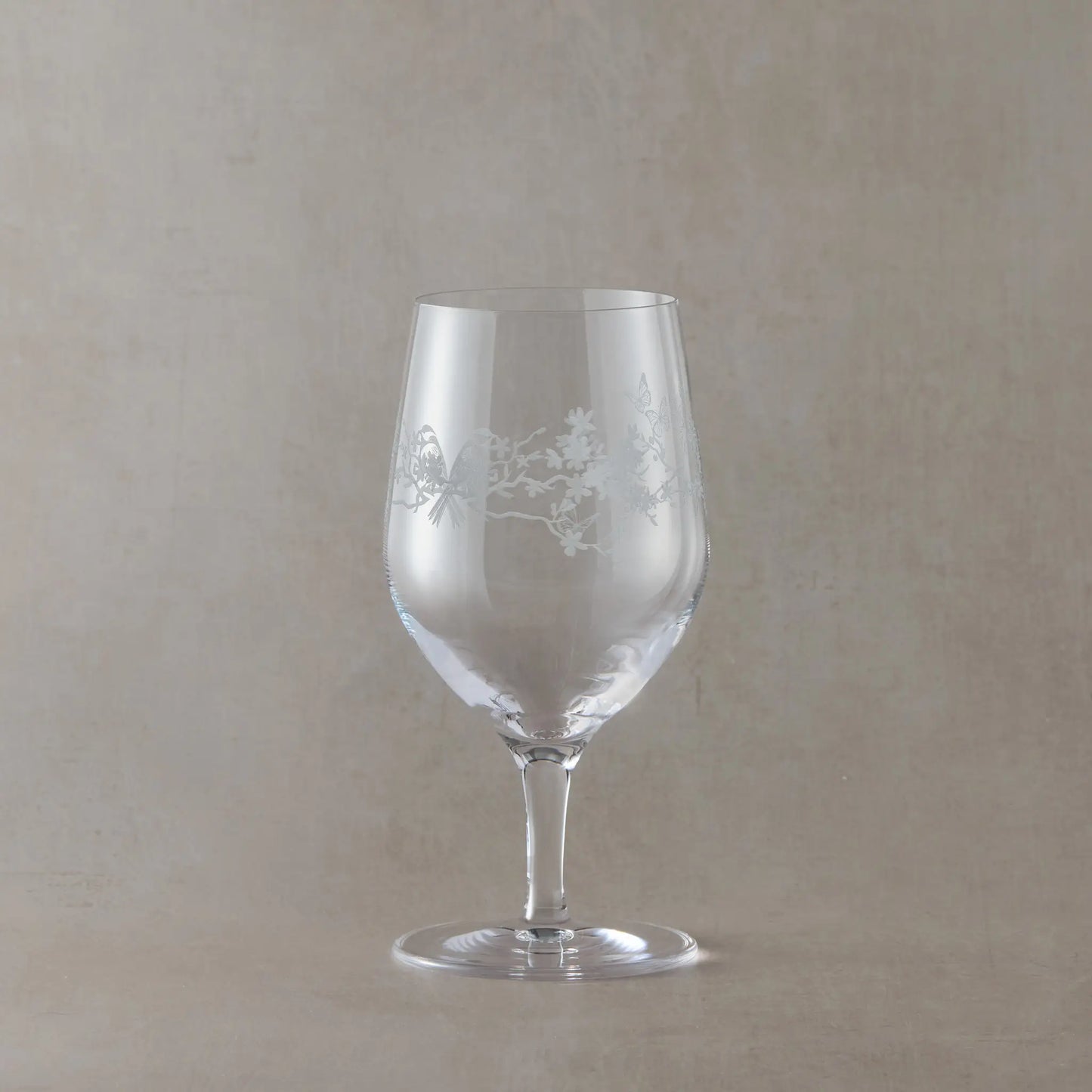 Mineral water glass with floral etching on a beige background