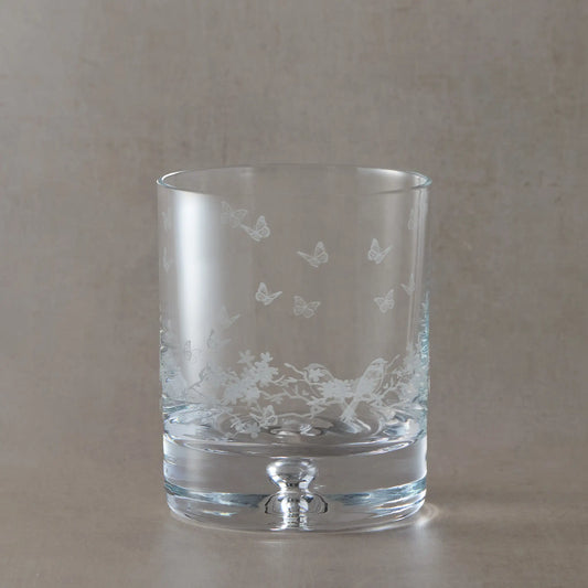 Engraved Le Jardin whisky glass with wraparound floral garland, garden birds and butterflies on a beige background